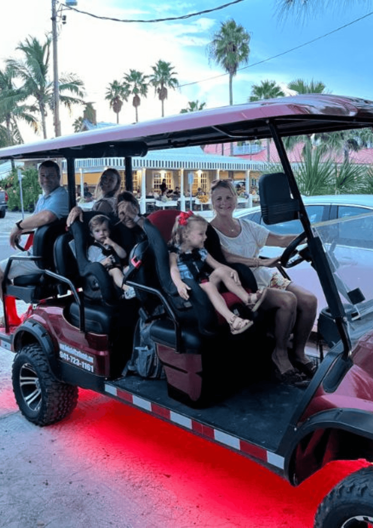 Family with young children in a maroon Hodo's golf cart at dusk